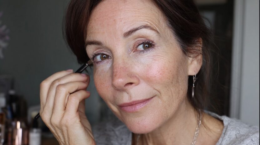 Middle-aged woman applying eyeliner with a soft smile, showing a natural, minimal makeup look