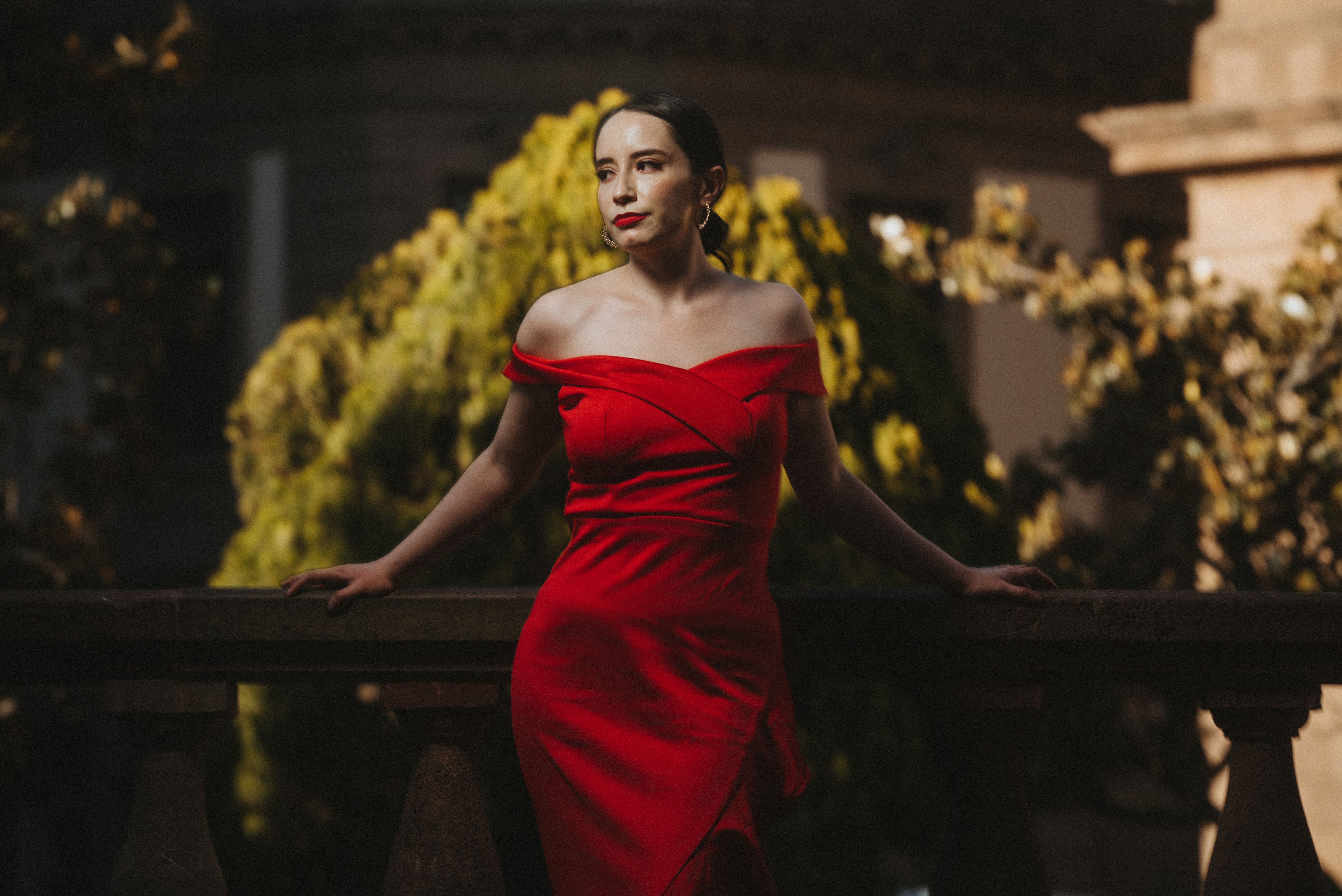 Woman in an elegant red dress posing on a balcony, showcasing sophisticated formalwear.