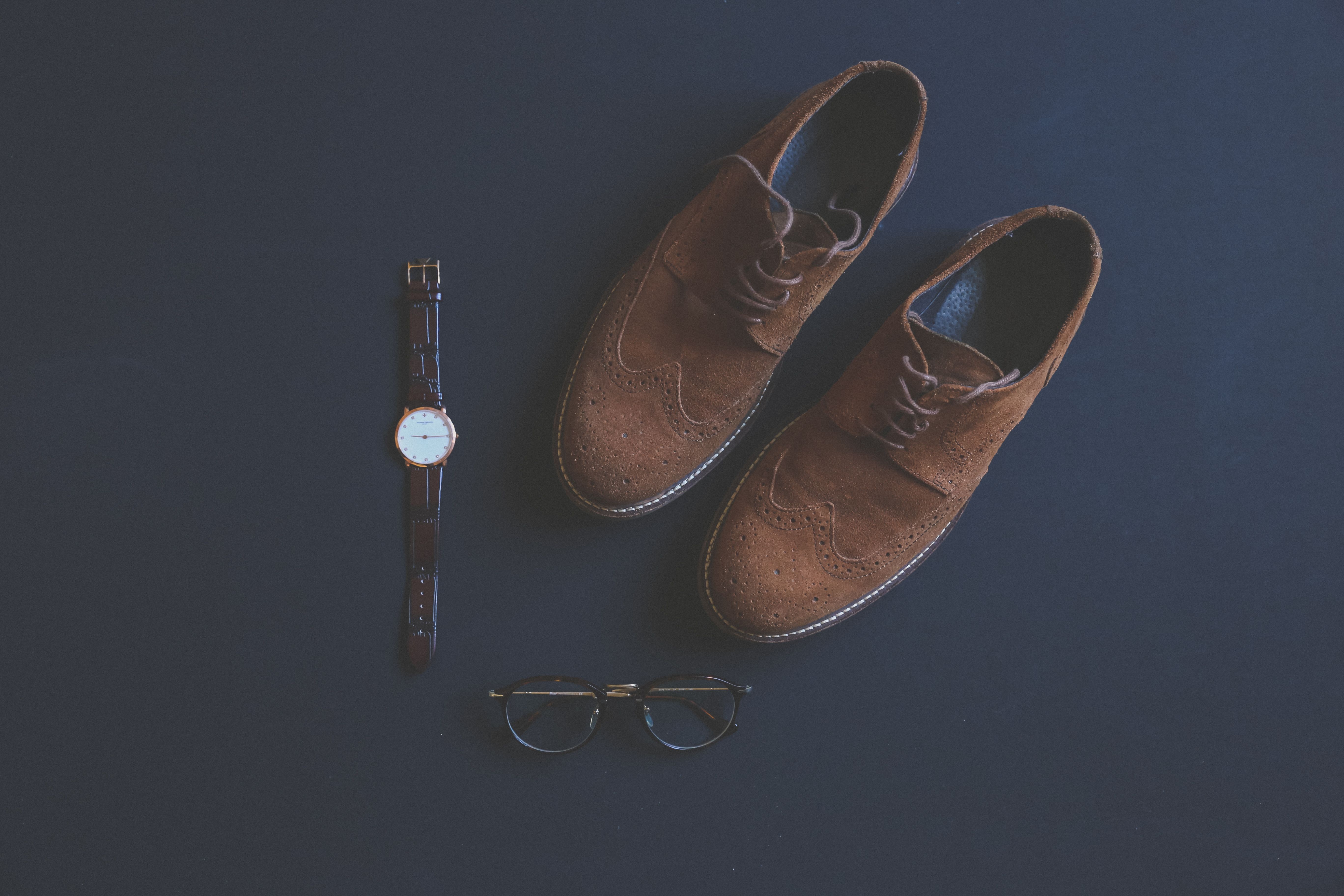 Leather shoes, eyeglasses, and a wristwatch arranged as classic outfit accessories.