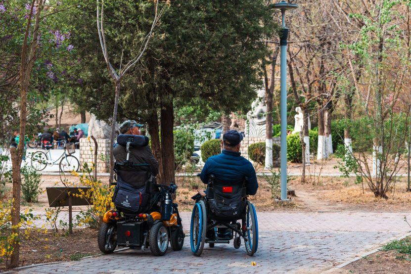 Two adults in wheelchairs enjoying a stroll through a scenic park in spring