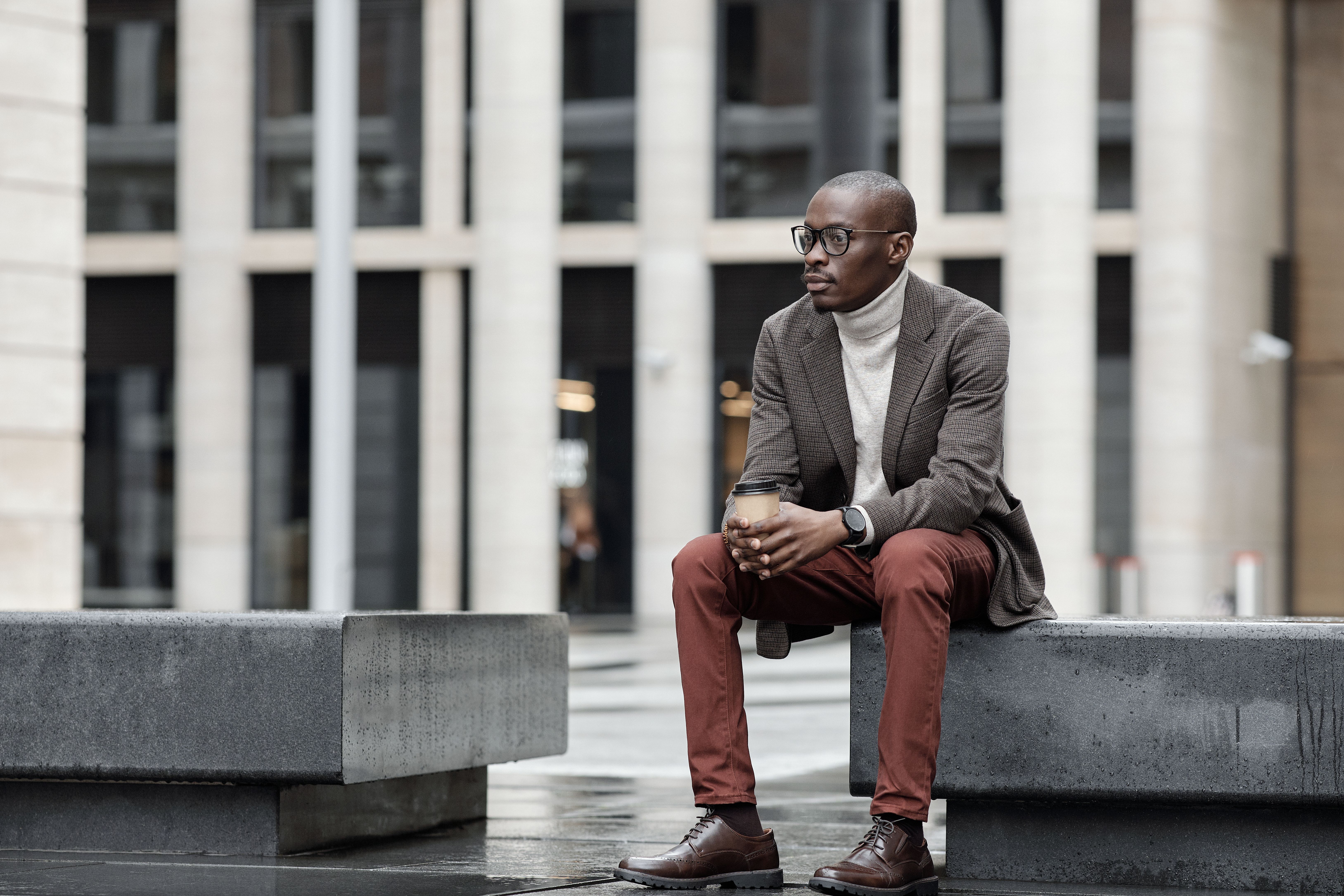 Fashionable man in smart casual clothing holding coffee in an urban setting.