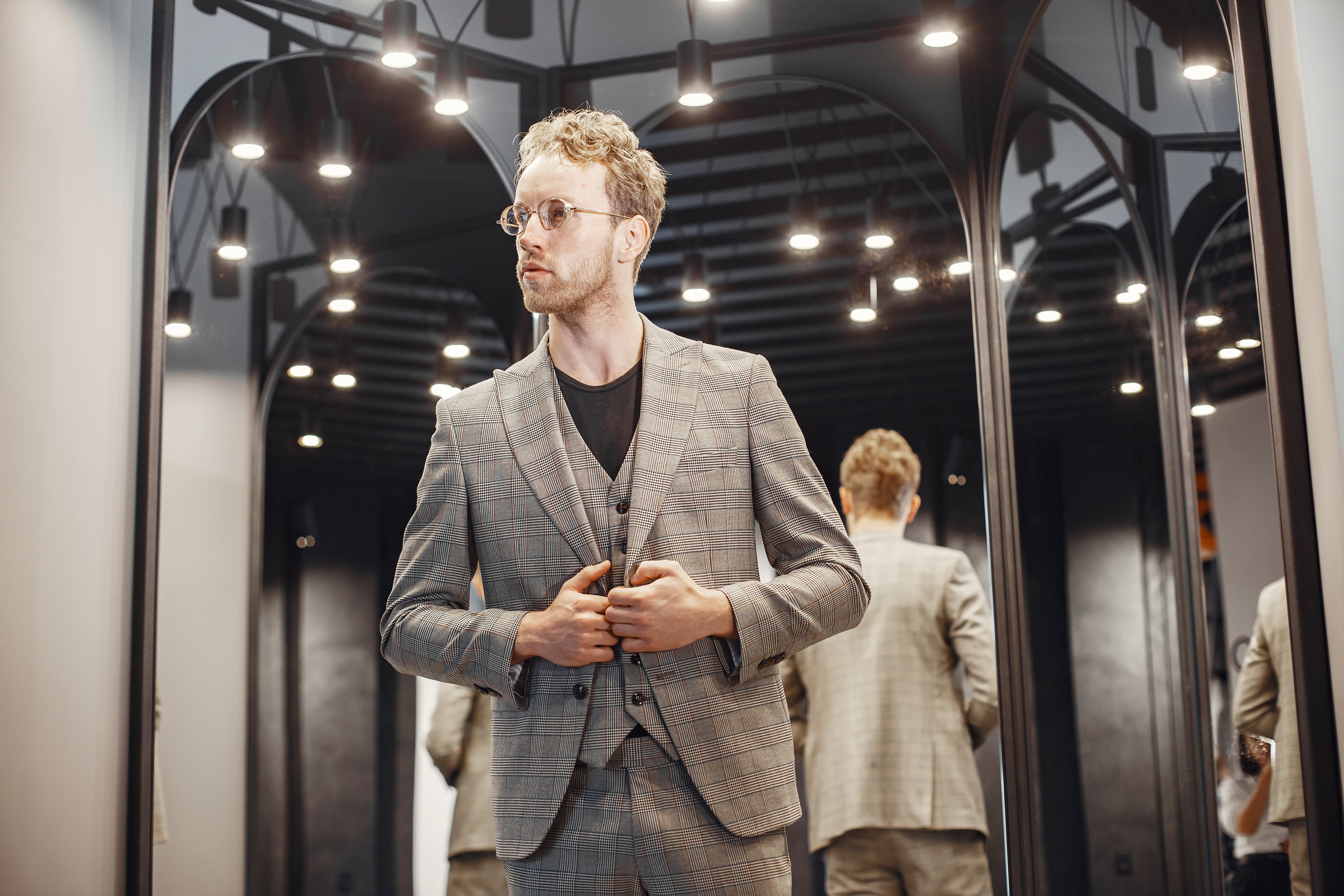 Elegant young man adjusting his suit in a dressing room, illustrating the importance of a polished fit.